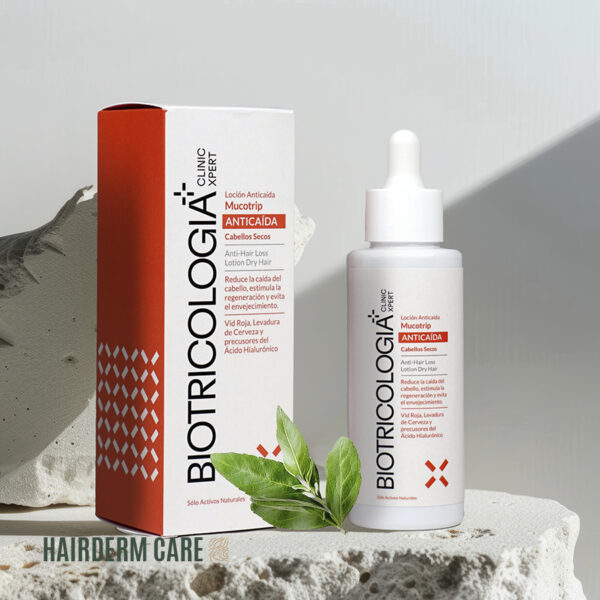 Imagen de un envase blanco con gotero y una caja anaranjada de "Loción Anticaída Mucotrip de Biotricología+" para cabellos secos. El diseño incluye texto promocional sobre las propiedades anticaída y revitalizantes del producto, destacando ingredientes naturales como Vino Rojo, Levadura de Cerveza y Ácido Hialurónico. Está situado sobre un fondo neutro con elementos naturales como hojas verdes, enfatizando su enfoque en ingredientes de origen natural.