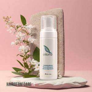 Envase de Mousse para el pelo Higienizante de Criloma de 150 ml, ideal para la limpieza y cuidado del cuero cabelludo y piel tras procedimientos quirúrgicos, mostrado junto a flores y sobre un fondo rosa.